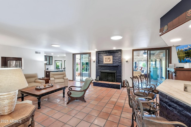 living room featuring a stone fireplace, ceiling fan, and light tile patterned floors