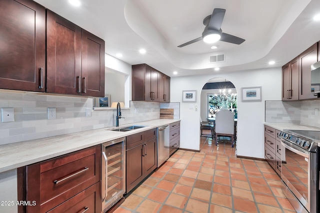 kitchen with sink, stainless steel appliances, tasteful backsplash, wine cooler, and ceiling fan with notable chandelier