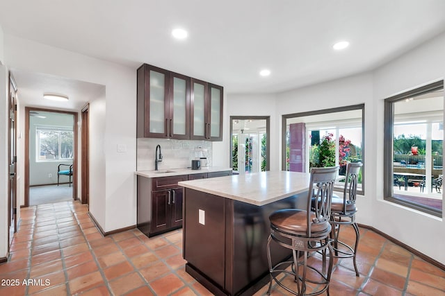 kitchen with sink, a kitchen breakfast bar, backsplash, dark brown cabinets, and a kitchen island