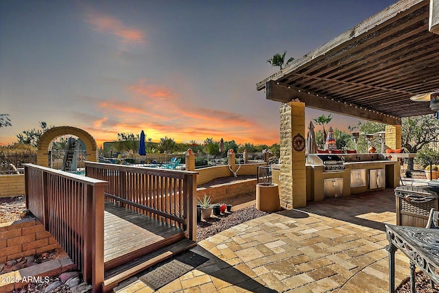 deck at dusk featuring grilling area, a patio area, and an outdoor kitchen