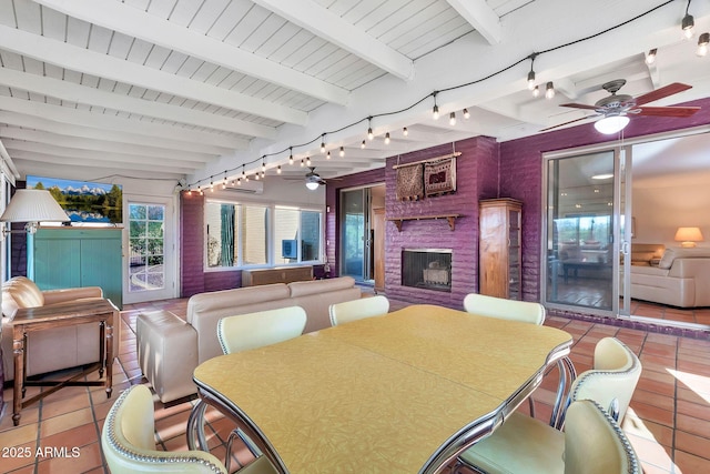 tiled dining space featuring track lighting, a brick fireplace, ceiling fan, beam ceiling, and wooden ceiling