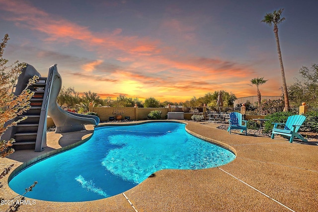 pool at dusk featuring a patio area and a water slide