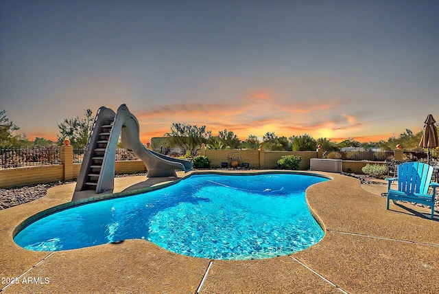 pool at dusk with a patio area and a water slide