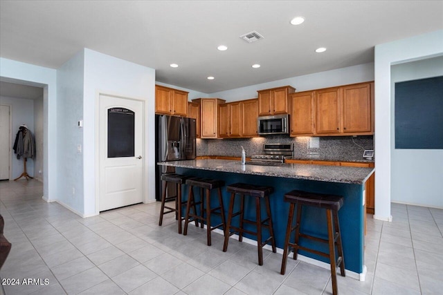 kitchen featuring an island with sink, tasteful backsplash, stainless steel appliances, and a breakfast bar area