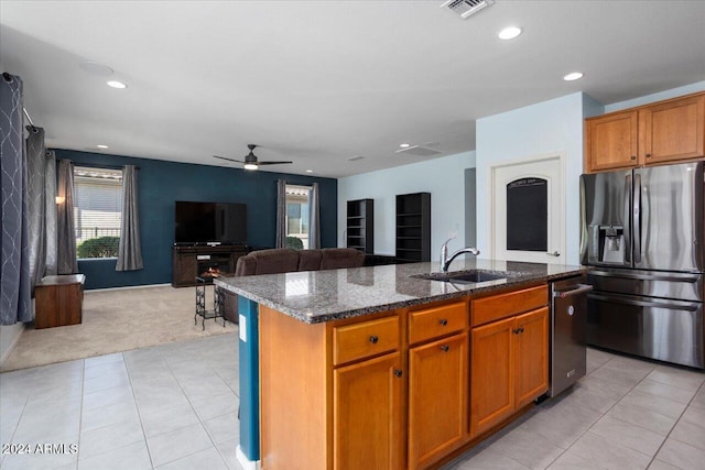 kitchen featuring appliances with stainless steel finishes, a kitchen island with sink, dark stone countertops, sink, and light colored carpet