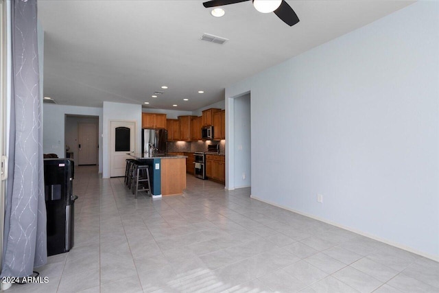 kitchen featuring tasteful backsplash, light tile patterned flooring, a kitchen breakfast bar, stainless steel appliances, and a center island with sink