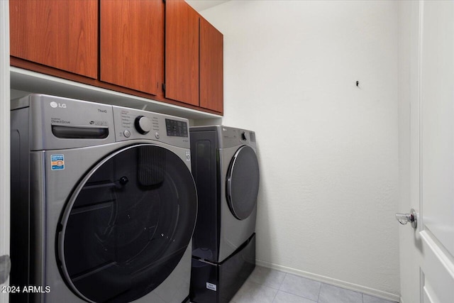 clothes washing area featuring cabinets, washer and dryer, and light tile patterned floors