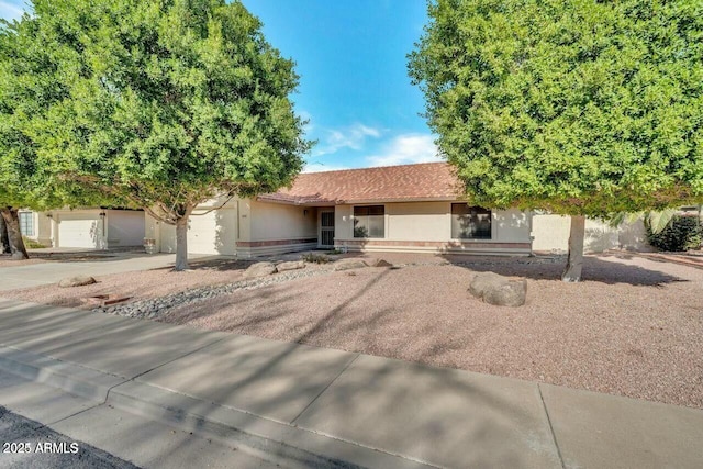 ranch-style home with concrete driveway, a tiled roof, an attached garage, and stucco siding