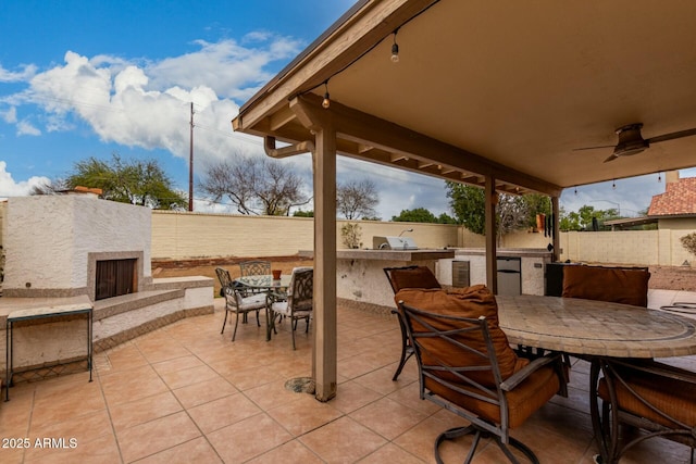 view of patio featuring outdoor dining area, a fenced backyard, an outdoor stone fireplace, a ceiling fan, and exterior kitchen