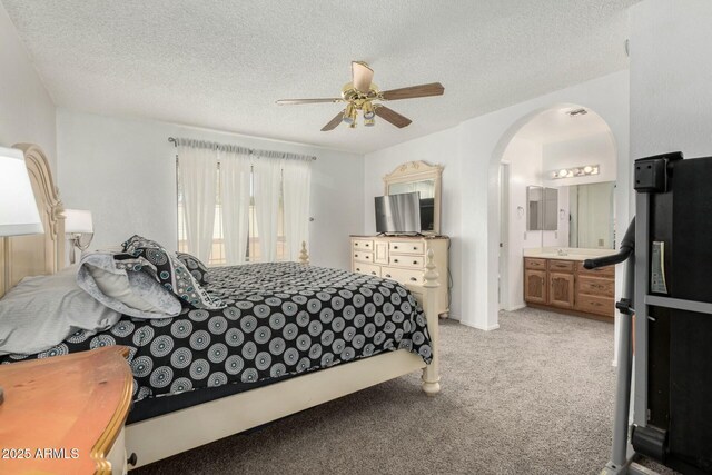 bedroom with light carpet, arched walkways, a ceiling fan, connected bathroom, and a textured ceiling