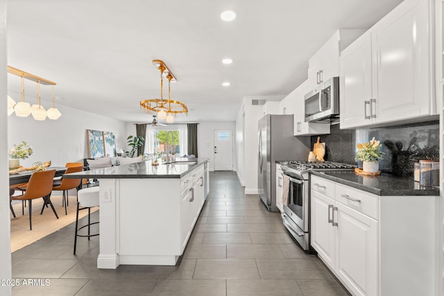 kitchen with white cabinetry, appliances with stainless steel finishes, backsplash, an island with sink, and dark countertops