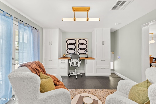 office area with dark wood-style floors, baseboards, visible vents, and built in desk