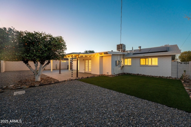 view of front of property featuring a fenced backyard, solar panels, brick siding, a yard, and a patio area