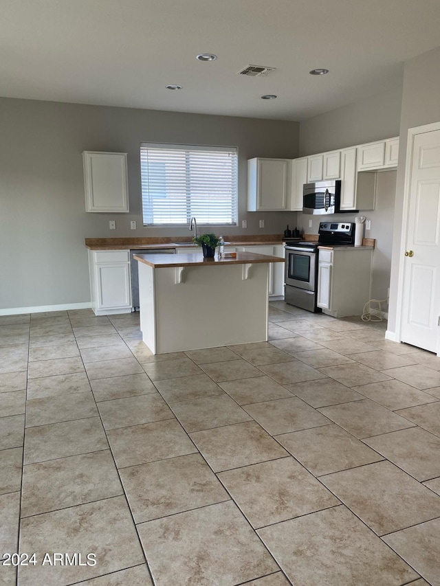 kitchen with a kitchen island, appliances with stainless steel finishes, light tile patterned floors, and white cabinets