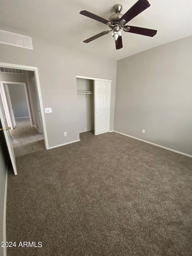 unfurnished bedroom with ceiling fan, dark carpet, and a closet