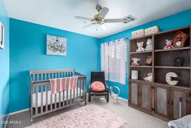 bedroom featuring a crib, light colored carpet, and ceiling fan