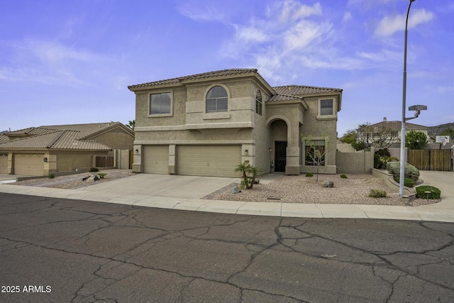 mediterranean / spanish house featuring an attached garage, fence, a tile roof, concrete driveway, and stucco siding