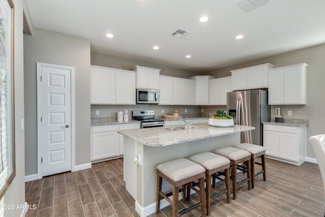 kitchen featuring an island with sink, wood-type flooring, white cabinets, and appliances with stainless steel finishes