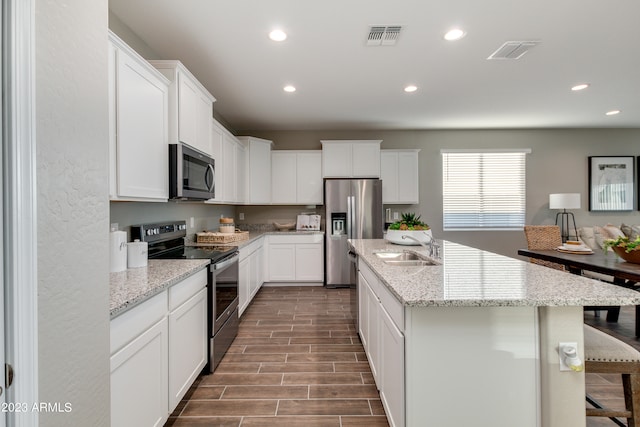 kitchen with stainless steel appliances, wood-type flooring, sink, an island with sink, and white cabinetry