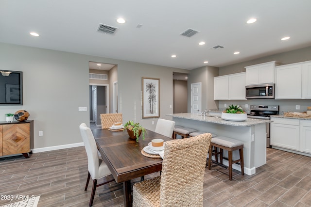 kitchen with hardwood / wood-style floors, white cabinetry, a kitchen island with sink, and stainless steel appliances