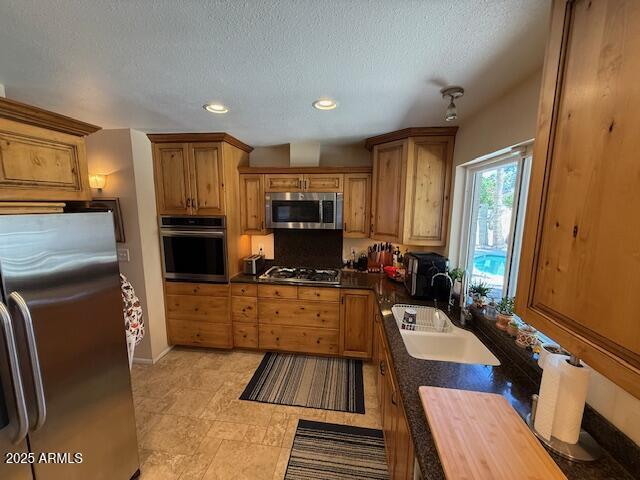 12601 N 34th St, Phoenix, AZ 85032 - kitchen featuring a textured ceiling, dark countertops, brown cabinetry, stainless steel appliances, and a sink