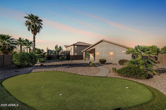 19576 N Portarosa Ct, Maricopa, AZ 85138 - view of front of property with a putting green, a trampoline, stucco siding, a fenced backyard, and a patio