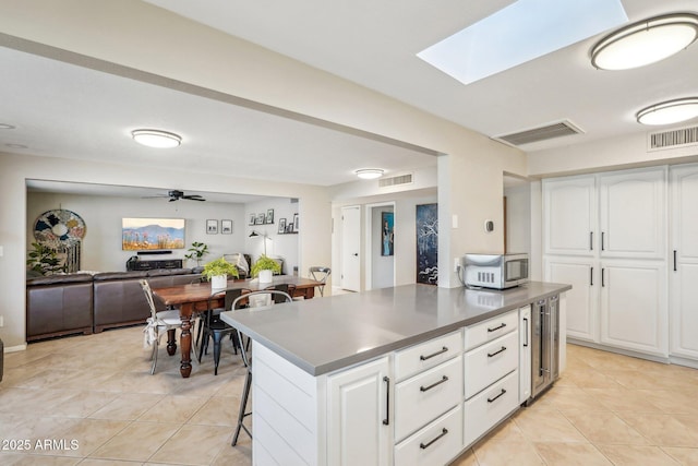 kitchen with a center island, white cabinets, a skylight, ceiling fan, and light tile patterned floors