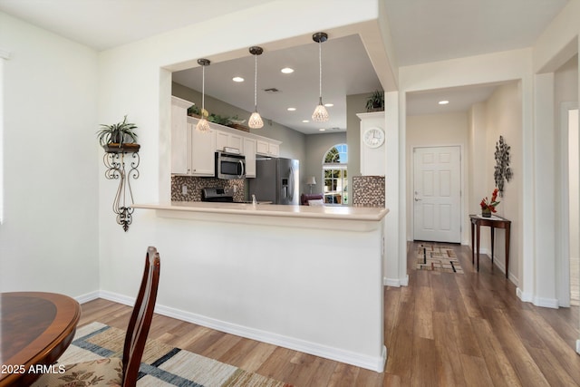 kitchen with wood finished floors, a peninsula, stainless steel appliances, white cabinetry, and tasteful backsplash