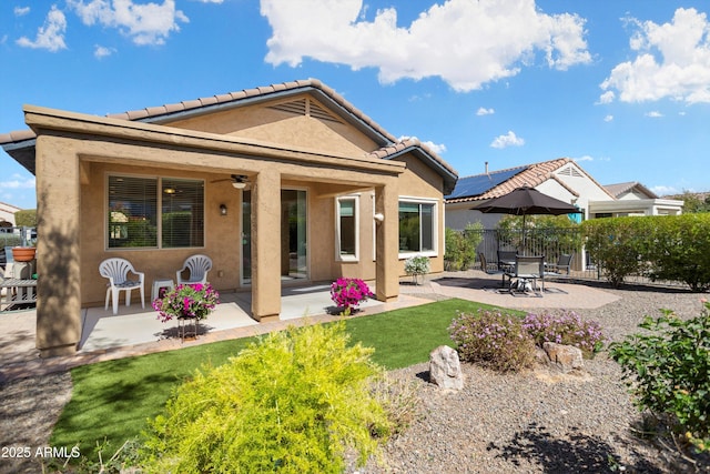 back of property with ceiling fan, fence, stucco siding, a lawn, and a patio