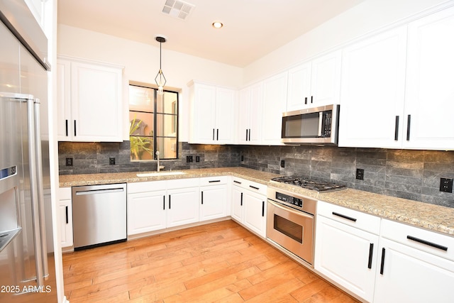 kitchen featuring pendant lighting, white cabinets, stainless steel appliances, tasteful backsplash, and sink