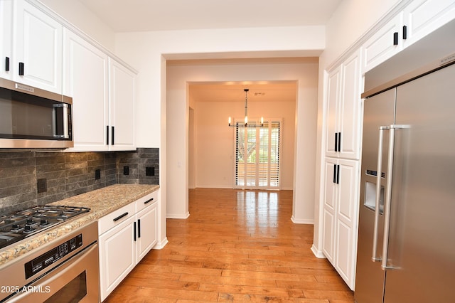 kitchen with tasteful backsplash, pendant lighting, stainless steel appliances, white cabinets, and light stone counters