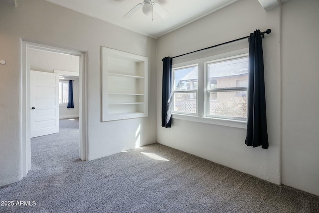 empty room featuring carpet flooring, built in shelves, and ceiling fan