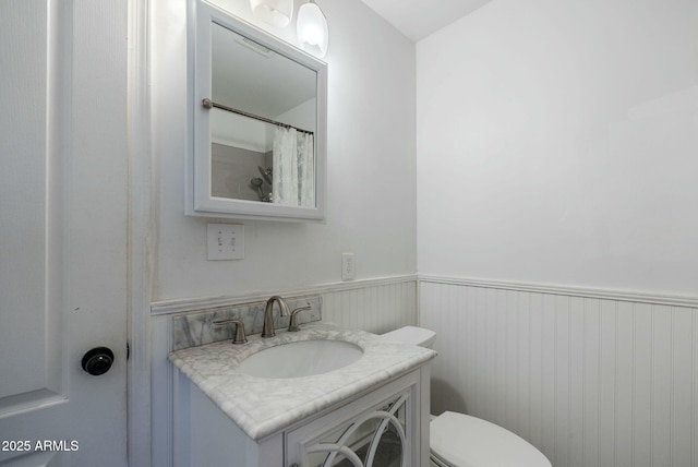 bathroom featuring vanity, toilet, and wainscoting