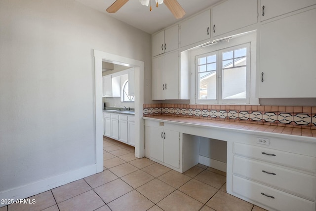 kitchen featuring a ceiling fan, a sink, white cabinets, built in desk, and tasteful backsplash