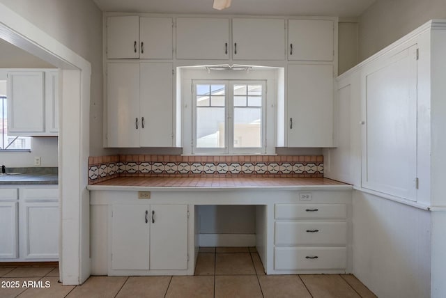 kitchen with backsplash, white cabinets, light tile patterned flooring, and built in study area