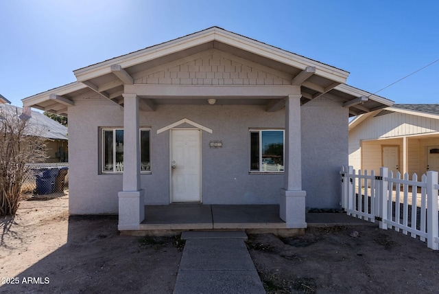 bungalow featuring stucco siding and fence