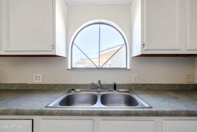 kitchen with dark countertops, white cabinetry, and a sink