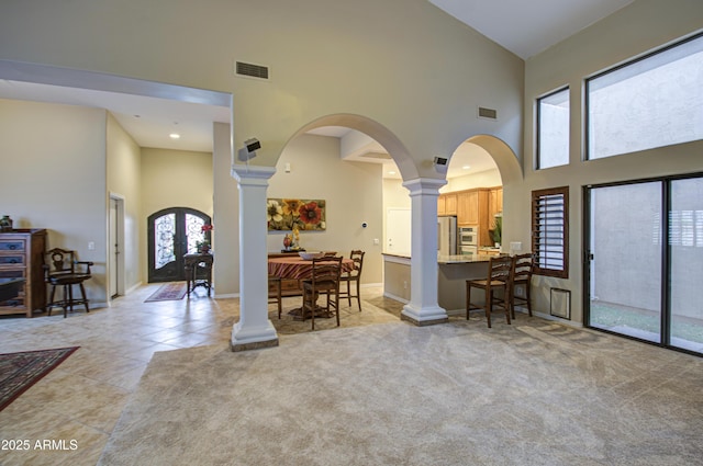 entrance foyer featuring visible vents, light colored carpet, ornate columns, and a towering ceiling