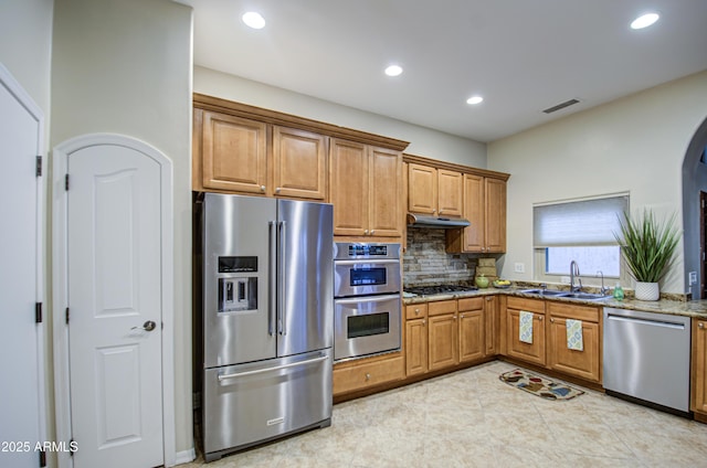 kitchen with visible vents, under cabinet range hood, light stone counters, stainless steel appliances, and a sink