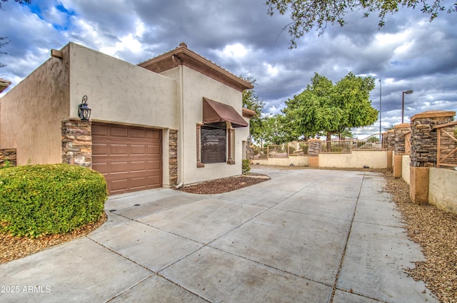 view of side of home featuring stucco siding, an attached garage, concrete driveway, and fence