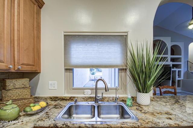 kitchen with a sink, light stone countertops, and brown cabinetry