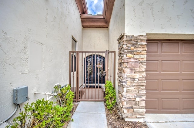 doorway to property with a garage, stone siding, stucco siding, and a gate