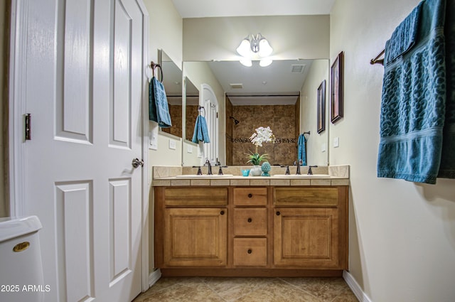 bathroom with double vanity, visible vents, a tile shower, and a sink