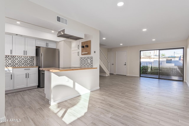 kitchen with white cabinets, stainless steel fridge, tasteful backsplash, and light hardwood / wood-style flooring