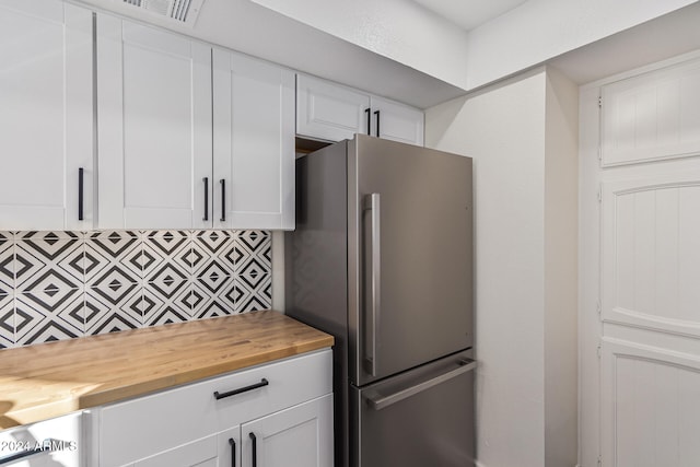 kitchen featuring stainless steel fridge, backsplash, white cabinetry, and butcher block counters