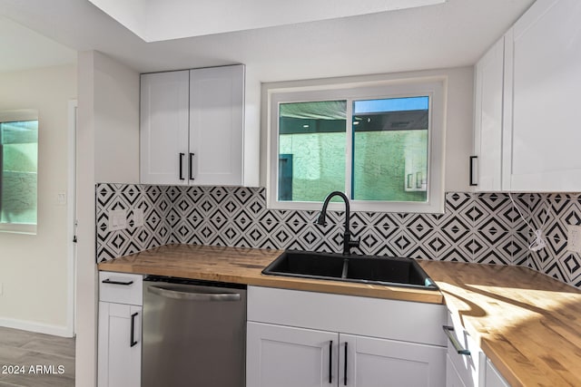 kitchen featuring butcher block countertops, stainless steel dishwasher, white cabinetry, and sink