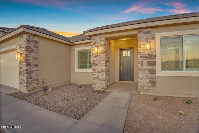 28319 N Marchant Trce, Queen Creek, AZ 85144 - exterior entry at dusk featuring stone siding, a garage, and stucco siding