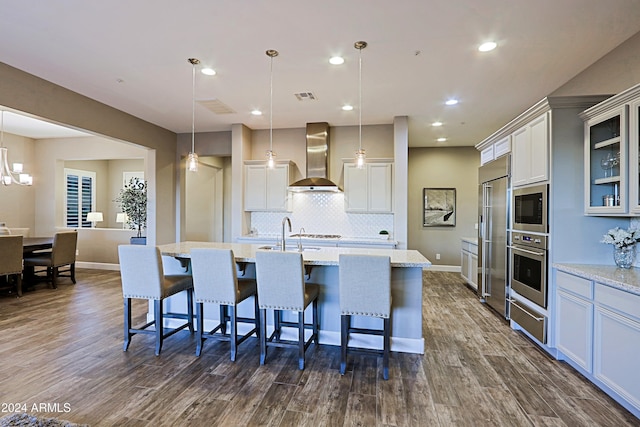 kitchen featuring built in appliances, wall chimney exhaust hood, dark hardwood / wood-style floors, and hanging light fixtures