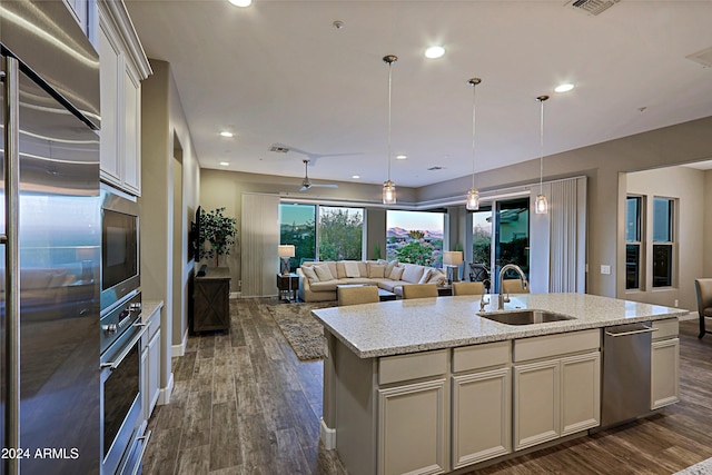 kitchen featuring light stone countertops, sink, dark hardwood / wood-style floors, a kitchen island with sink, and appliances with stainless steel finishes