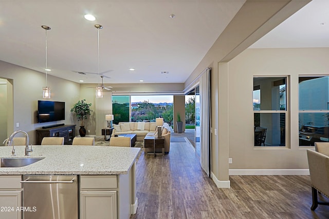 kitchen with sink, light stone counters, stainless steel dishwasher, dark hardwood / wood-style floors, and pendant lighting